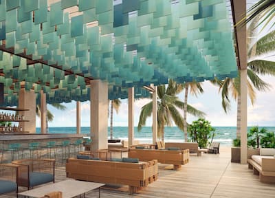 An outside bar area looking out to a palm tree-lined beach with the ocean in the background.