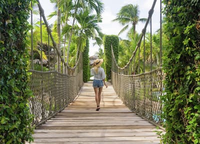 Woman walking across rope bridge, surrounded by palm trees