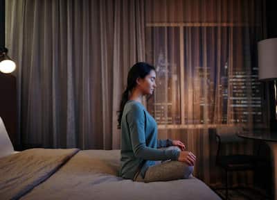 A girl sitting crossed legged on a bed in a dimly-lit room while meditating.