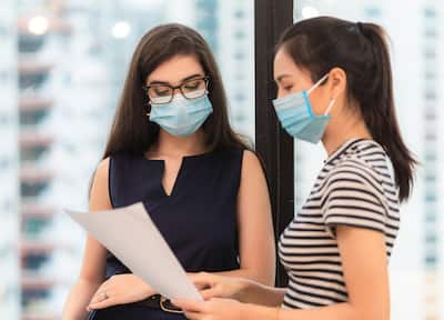 Two women wearing masks looking down at a piece of paper
