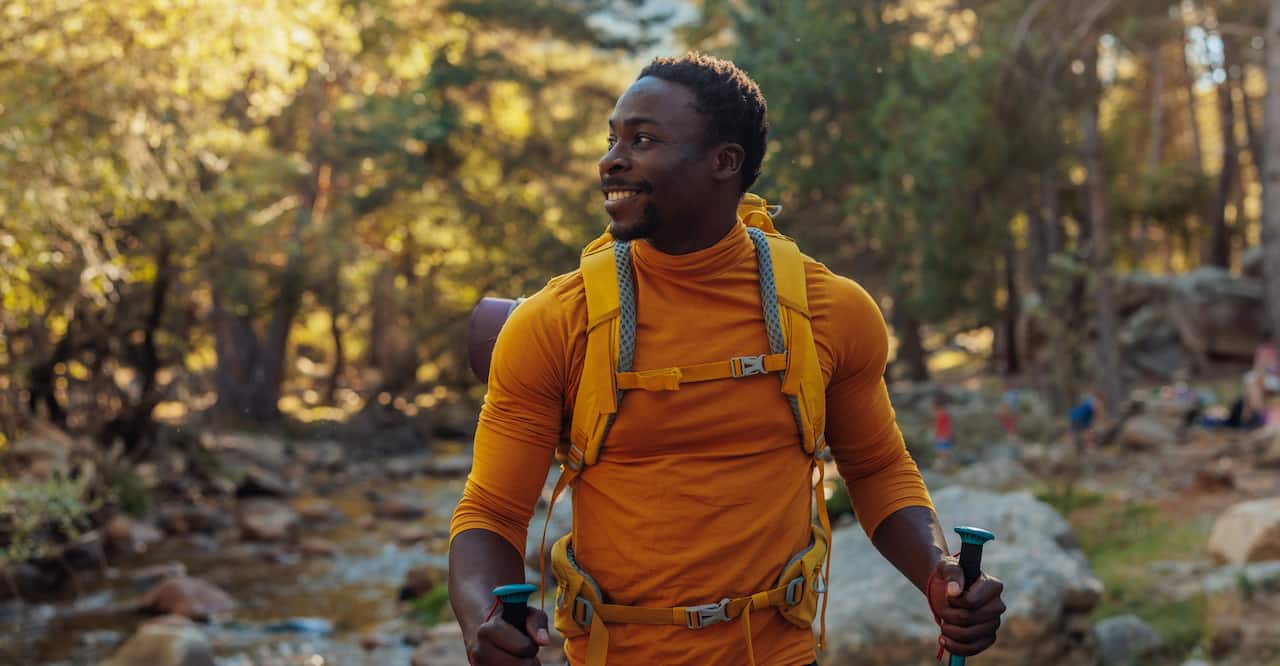 A cheerful African American hiker is standing next to a mountain stream in the forest.