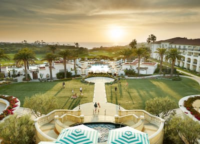 aerial view of hotel exterior and grounds with pools, view of golf course, and people walking